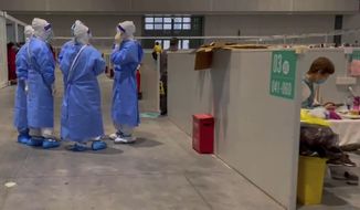 In this image taken from a video provided by Beibei, who asked to be identified only by her given name, medical workers wearing protective suits chat as a resident takes a rest at the National Exhibition and Convention Center on April 15, 2022, in Shanghai. The convention center was converted to a quarantine facility set up for people who tested positive but have few or no symptoms. (Beibei via AP)
