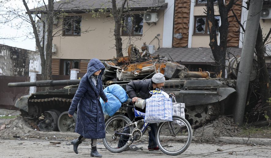 Local civilians walk past a tank destroyed during heavy fighting in an area controlled by Russian-backed separatist forces in Mariupol, Ukraine, Tuesday, April 19, 2022. Taking Mariupol would deprive Ukraine of a vital port and complete a land bridge between Russia and the Crimean Peninsula, seized from Ukraine from 2014. (AP Photo/Alexei Alexandrov)