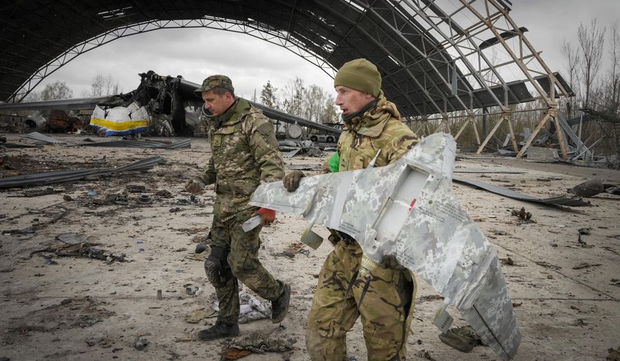Ukrainian sappers carry a Russian military drone backdropped by the Antonov An-225, world&#39;s biggest cargo aircraft destroyed by the Russian troops during recent fighting, at the Antonov airport in Hostomel, on the outskirts of Kyiv, Ukraine, Monday, April 18, 2022. (AP Photo/Efrem Lukatsky)