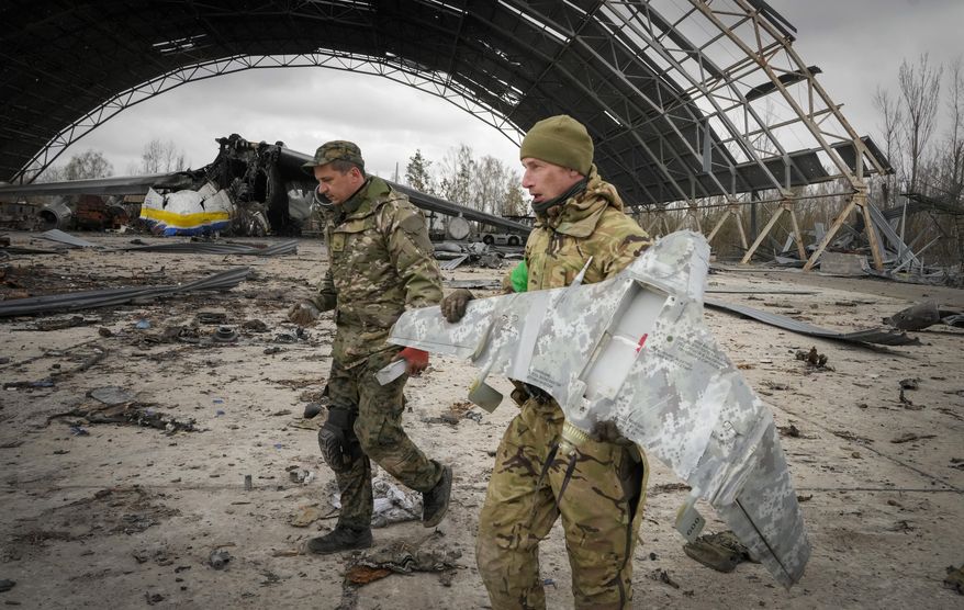 Ukrainian sappers carry a Russian military drone backdropped by the Antonov An-225, world&#39;s biggest cargo aircraft destroyed by the Russian troops during recent fighting, at the Antonov airport in Hostomel, on the outskirts of Kyiv, Ukraine, Monday, April 18, 2022. (AP Photo/Efrem Lukatsky)
