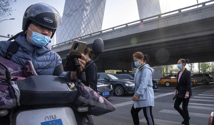 Commuters wearing face masks walk across an intersection in the central business district in Beijing, Tuesday, April 19, 2022. (AP Photo/Mark Schiefelbein)