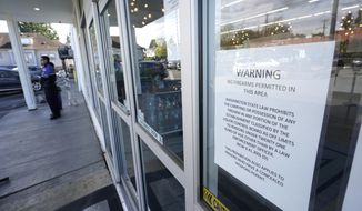 A sign warns that firearms are prohibited at Mary Mart, a marijuana store, Tuesday, April 19, 2022, in Tacoma, Wash., as armed security guard Austin MacMath stands watch outside at left. A surge in robberies at licensed cannabis shops in Washington state is helping fuel a renewed push for federal banking reforms that would make the cash-dependent stores a less appealing target. (AP Photo/Ted S. Warren)