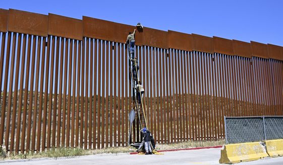 People use a ladder to scale the border fence at the US/Mexico border in Tecate, Mexico, Thursday, April 21, 2022. The men used the ropes to lower themselves down on the United States side. (AP Photo/Denis Poroy)