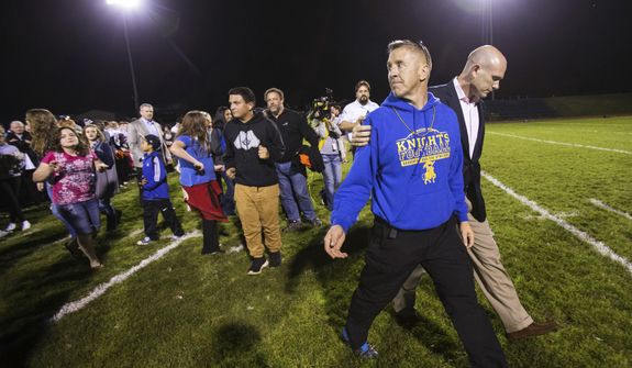 Bremerton High assistant football coach Joe Kennedy, front, walks off the field with his lawyer, right, Oct. 16, 2015, after praying at the 50-yard line following a football game in Bremerton, Wash. After losing his coaching job for refusing to stop kneeling in prayer with players and spectators on the field immediately after football games, Kennedy will take his arguments before the U.S. Supreme Court on Monday, April 25, 2022, saying the Bremerton School District violated his First Amendment rights by refusing to let him continue praying at midfield after games. (Lindsey Wasson/The Seattle Times via AP) **FILE**