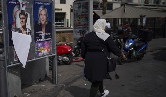 A woman walks by presidential campaign posters in Marseille, southern France, Wednesday, April 13, 2022. Marine Le Pen’s vision for France if the far-right leader wins Sunday’s runoff presidential election would include a ban on Muslim headscarves in public, schoolchildren in uniforms and laws passed by referendum. (AP Photo/Daniel Cole, File)