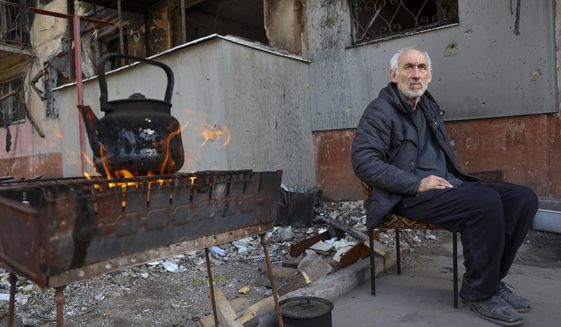 A local man sits in front of an apartment building damaged from heavy fighting as he waits for the kettle to boil in an area controlled by Russian-backed separatist forces in Mariupol, Ukraine, Tuesday, April 26, 2022. (AP Photo/Alexei Alexandrov)