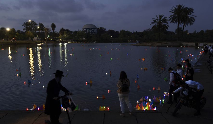 People look on floating handmade boats lit with candles and with the names of Nazi concentration camps, during a ceremony marking the annual Holocaust Remembrance Day in Hayarkon park in Tel Aviv, Israel, Wednesday, April 27, 2022. Israel marking the annual Day of Remembrance for the six million Jewish victims of the Nazi genocide who perished during World War II. (AP Photo/Oded Balilty)