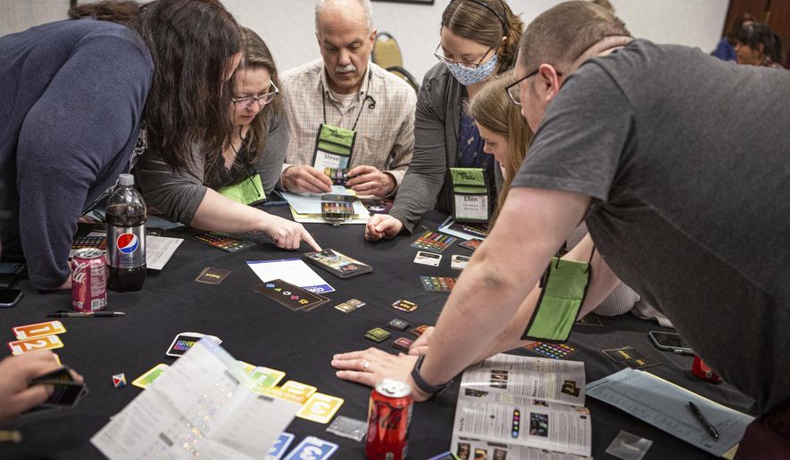 A group of Mensa members gather around a table, Thursday, April 28, 2022, during the American Mensa's Mind Games event in South Portland, Maine. Makers of board games are seeking the brainiac seal of approval this weekend, as Mensa members engage in round-the-clock gaming. (Troy R. Bennett/The Bangor Daily News via AP)