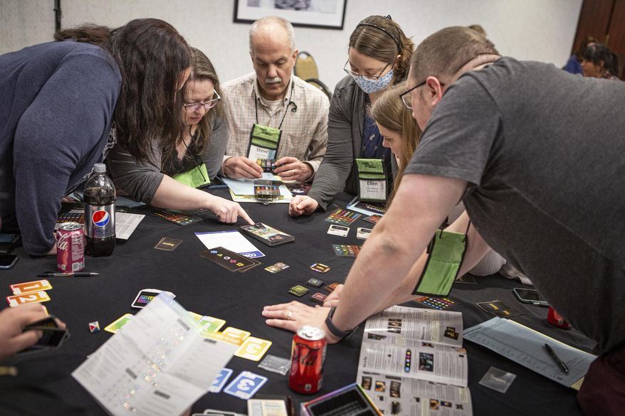 A group of Mensa members gather around a table, Thursday, April 28, 2022, during the American Mensa's Mind Games event in South Portland, Maine. Makers of board games are seeking the brainiac seal of approval this weekend, as Mensa members engage in round-the-clock gaming. (Troy R. Bennett/The Bangor Daily News via AP)
