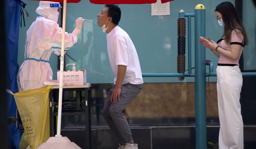 A worker wearing a protective suit swabs a man's throat for a COVID-19 test at a testing site during the second consecutive day of mass testing in Beijing, Wednesday, May 4, 2022. Beijing on Wednesday closed around 10% of the stations in its vast subway system as an additional measure against the spread of coronavirus. (AP Photo/Mark Schiefelbein)