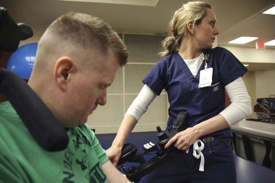 FILE - In this July 6, 2017 photo, occupational therapist Ashley Broadwater, waits for help to sit Cpl. Nick Tullier on a bed so he can begin his physical rehabilitation at TIRR Memorial Hermann Hospital in Houston. Tullier, a Baton Rouge sheriff’s deputy who was shot in the head and stomach during a July 2016 ambush that killed three other law enforcement officers during a summer of protests over the police killing of a Black man, died Thursday, May 5, 2022, at age 47. Tullier's death was announced on the Facebook page of his father, James Tullier, and on a companion page dedicated to Tullier's effort to recover in the years since the shooting. (AP Photo/John L. Mone)