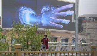 A woman talks on her phone near a screen depicting a giant hand at an empty mall area with closed retail shops and restaurants only offering takeaway on Tuesday, May 10, 2022, in Beijing. China&#39;s capital began another round of three days of mass testing for millions of its residents Tuesday in a bid to prevent an outbreak from growing to Shanghai proportions. (AP Photo/Ng Han Guan)