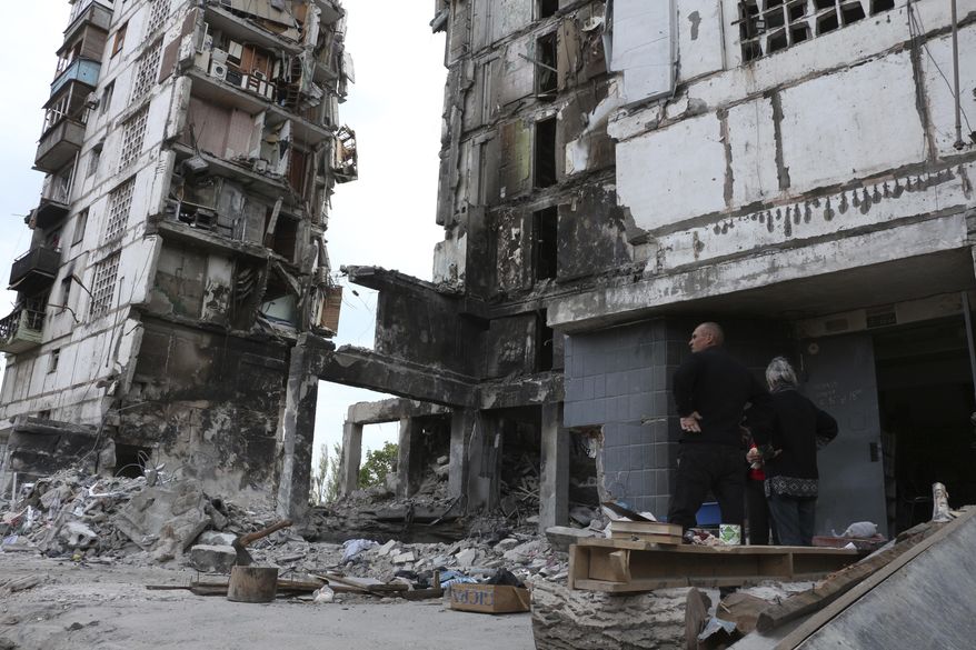 Local residents stand at the side of damaged during a heavy fighting buildings in Mariupol, in territory under the government of the Donetsk People&#39;s Republic, eastern Ukraine, Friday, May 13, 2022. (AP Photo)