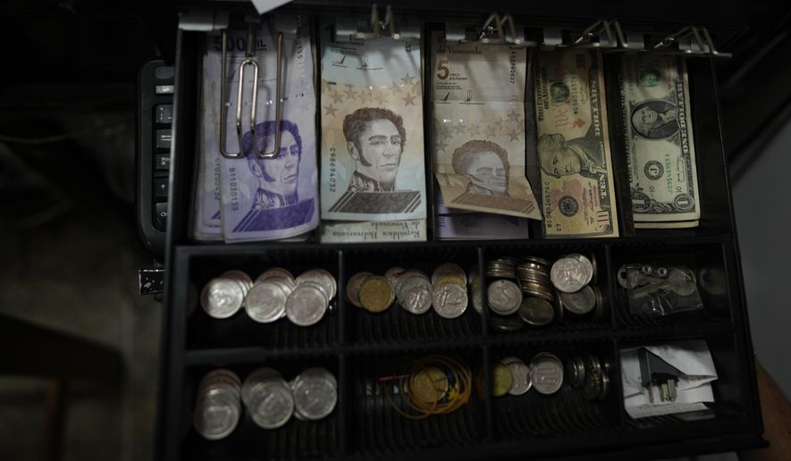 A cash register drawer holds Bolivars and U.S. currencies at a shop in Caracas, Venezuela, Friday, May 13, 2022. A new tax law approved by the Venezuelan government, that went into effect in March, applies a 3% tax charge on transactions paid in foreign currencies. (AP Photo/Ariana Cubillos)