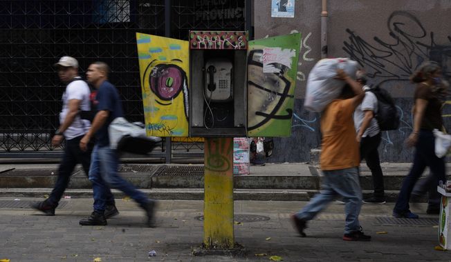 Pedestrians walk past an out of service National Telephone Company of Venezuela, CANTV, phone booth, in Caracas,Venezuela, Friday, May 13, 2022. A number of Venezuelan state-owned companies, including in the telecommunications sector, will sell up to 10% of their shares starting Monday. President Nicolas Maduro says the companies will be listed in the country&#x27;s stock exchange and the sale is open to local and foreign investors. (AP Photo/Ariana Cubillos)