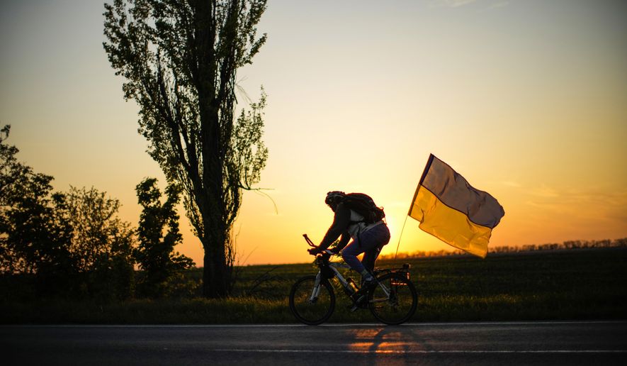 A man rides a bicycle with a Ukrainian flag on the road between Odesa and Mykolaiv, southern Ukraine, Saturday, May 14, 2022. (AP Photo/Francisco Seco)