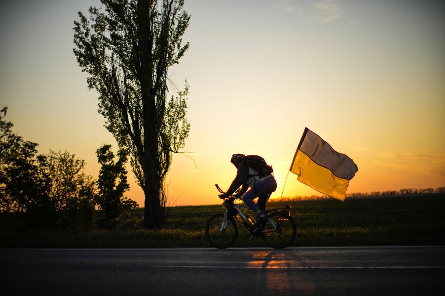 A man rides a bicycle with a Ukrainian flag on the road between Odesa and Mykolaiv, southern Ukraine, Saturday, May 14, 2022. (AP Photo/Francisco Seco)
