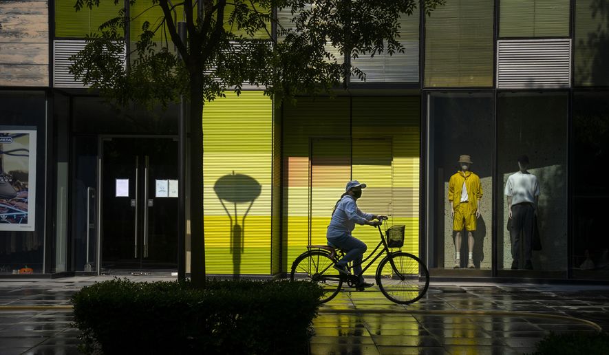 A woman wearing a face mask rides a bicycle past stores closed for COVID-19 control at a shopping mall in Beijing, Tuesday, May 17, 2022. (AP Photo/Mark Schiefelbein)