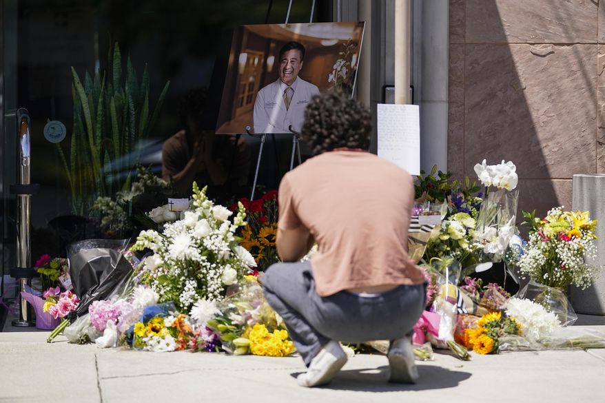 Gabe Kipers, a neighbor of Dr. John Cheng, kneels at a memorial for him outside his office building on Tuesday, May 17, 2022, in Aliso Viejo, Calif. Cheng, 52, was killed in Sunday's shooting at Geneva Presbyterian Church. (AP Photo/Ashley Landis)