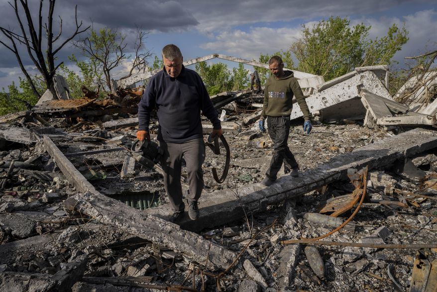 Villagers walk past unexploded artillery shells as they collect scrap metal from a bombed warehouse in the village of Malaya Rohan, Kharkiv region, Wednesday, May 18, 2022. (AP Photo/Bernat Armangue)