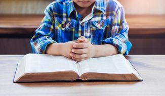A child praying on open Bible with blurred page on wooden table. (Photo credit: Freedom Studio via Shutterstock)