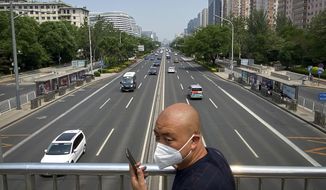 A man wearing a face mask stands on a bridge over an expressway in Beijing, Thursday, May 19, 2022. Parts of Beijing on Thursday halted daily mass testing that had been conducted over the past several weeks, but many testing sites remained busy due to requirements for a negative COVID test in the last 48 hours to enter some buildings in China&#39;s capital. (AP Photo/Mark Schiefelbein)