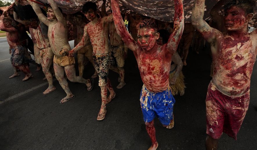 FILE - Indigenous people painted with red ink representing spilled Indigenous blood and clay representing gold, protest against the increase of mining activities that are encroaching on their land, in front of the Ministry of Mines and Energy, in Brasilia, Brazil, April 11, 2022. Some of the world’s biggest mining companies have withdrawn requests for research and production in Indigenous territories of Brazil’s Amazon rainforest, and have repudiated Brazilian President Jair Bolsonaro’s efforts to legalize mining activity in the areas. (AP Photo/Eraldo Peres, File)