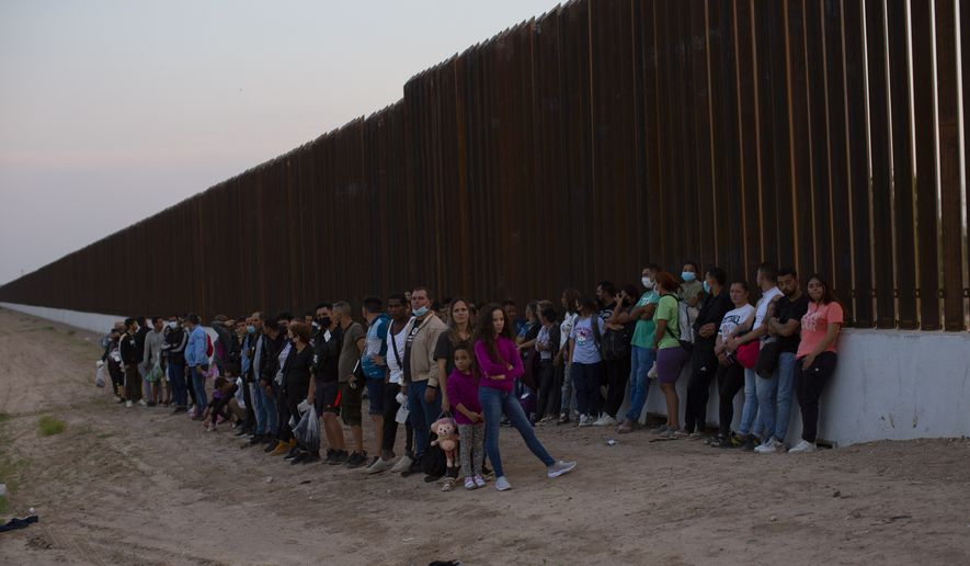 A group of migrants stand next to the border wall as they wait to get taken away by the Border Patrol in Eagle Pass, Texas, Saturday, May 21, 2022. The Eagle Pass area has become increasingly a popular crossing corridor for migrants, especially those from outside Mexico and Central America, under Title 42 authority, which expels migrants without a chance to seek asylum on grounds of preventing the spread of COVID-19. (AP Photo/Dario Lopez-Mills)