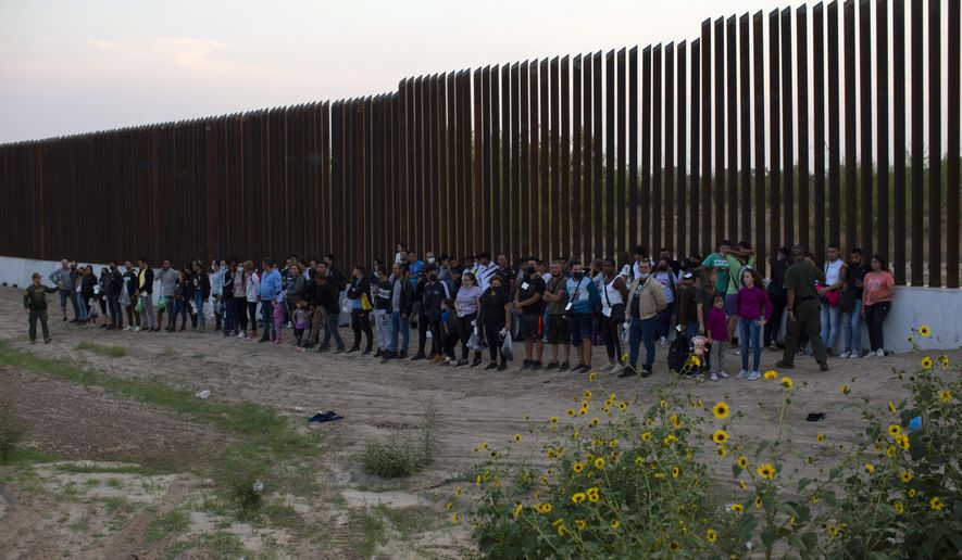 Migrants stand next to the border wall as they wait to get taken away by the Border Patrol in Eagle Pass, Texas, Saturday, May 21, 2022. The Eagle Pass area has become increasingly a popular crossing corridor for migrants, especially those from outside Mexico and Central America, under Title 42 authority, which expels migrants without a chance to seek asylum on grounds of preventing the spread of COVID-19. (AP Photo/Dario Lopez-Mills) ** FILE **