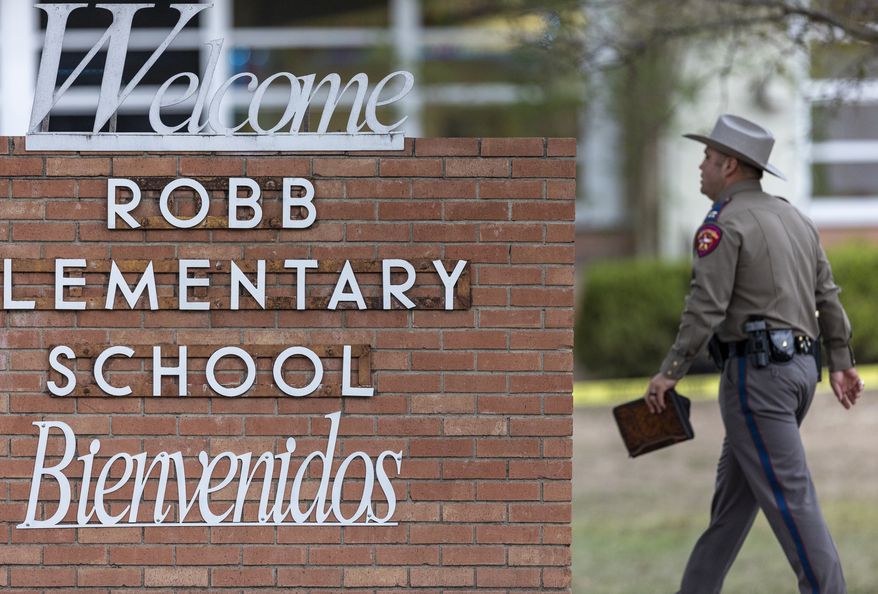 A state trooper walks past the Robb Elementary School sign in Uvalde, Texas, Tuesday, May 24, 2022, following a deadly shooting at the school. (William Luther/The San Antonio Express-News via AP)