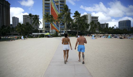 Honeymooners Samantha Hanberg, left, and Brian Swan walk along Waikiki Beach in Honolulu, Monday, May 23, 2022. A COVID surge is under way that is starting to cause disruptions as schools wrap up for the year and Americans prepare for summer vacations. Case counts are as high as they&#x27;ve been since mid-February and those figures are likely a major undercount because of unreported home tests and asymptomatic infections. But the beaches beckoned and visitors have flocked to Hawaii, especially in recent months. (AP Photo/Caleb Jones)