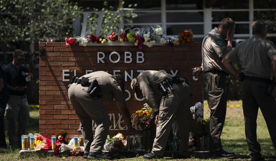 Two Texas Troopers light a candle at Robb Elementary School in Uvalde, Texas, Wednesday, May 25, 2022. Desperation turned to heart-wrenching sorrow for families of grade schoolers killed after an 18-year-old gunman barricaded himself in their Texas classroom and began shooting, killing several fourth-graders and their teachers. (AP Photo/Jae C. Hong)