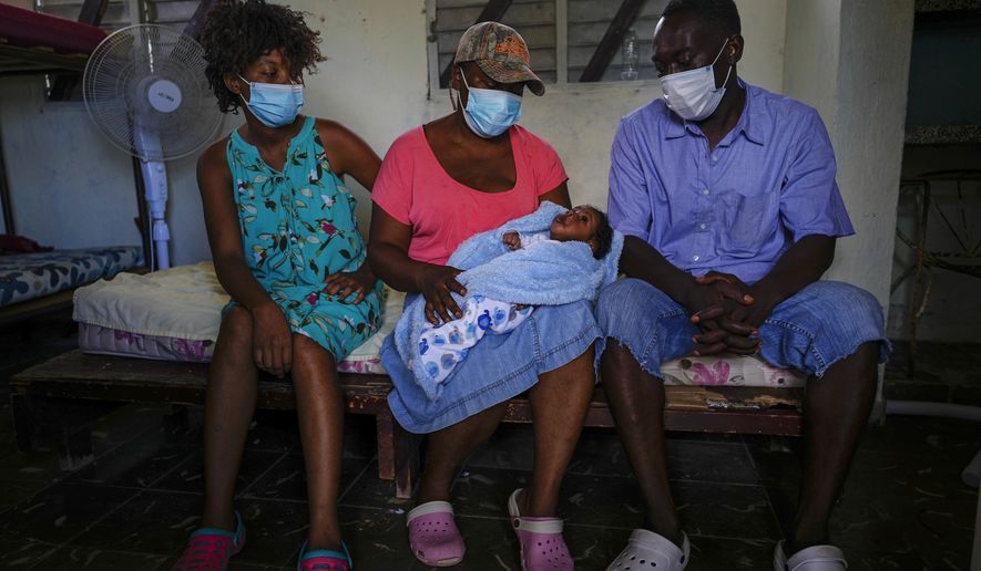 Loverie Horat, left, sits by her mother holding her 24-day-old daughter Maylie Dhavavaise as her husband Maximaud Cherizad looks on, at a campground being used to house the large group of Haitian migrants with whom they are traveling, in Sierra Morena in Cuba&#39;s Villa Clara province, Thursday, May 26, 2022. A vessel carrying more than 800 Haitians trying to reach the United States wound up instead on the coast of central Cuba, in what appeared to be the largest group seen yet in a swelling exodus from crisis-stricken Haiti. (AP Photo Ramon Espinosa)