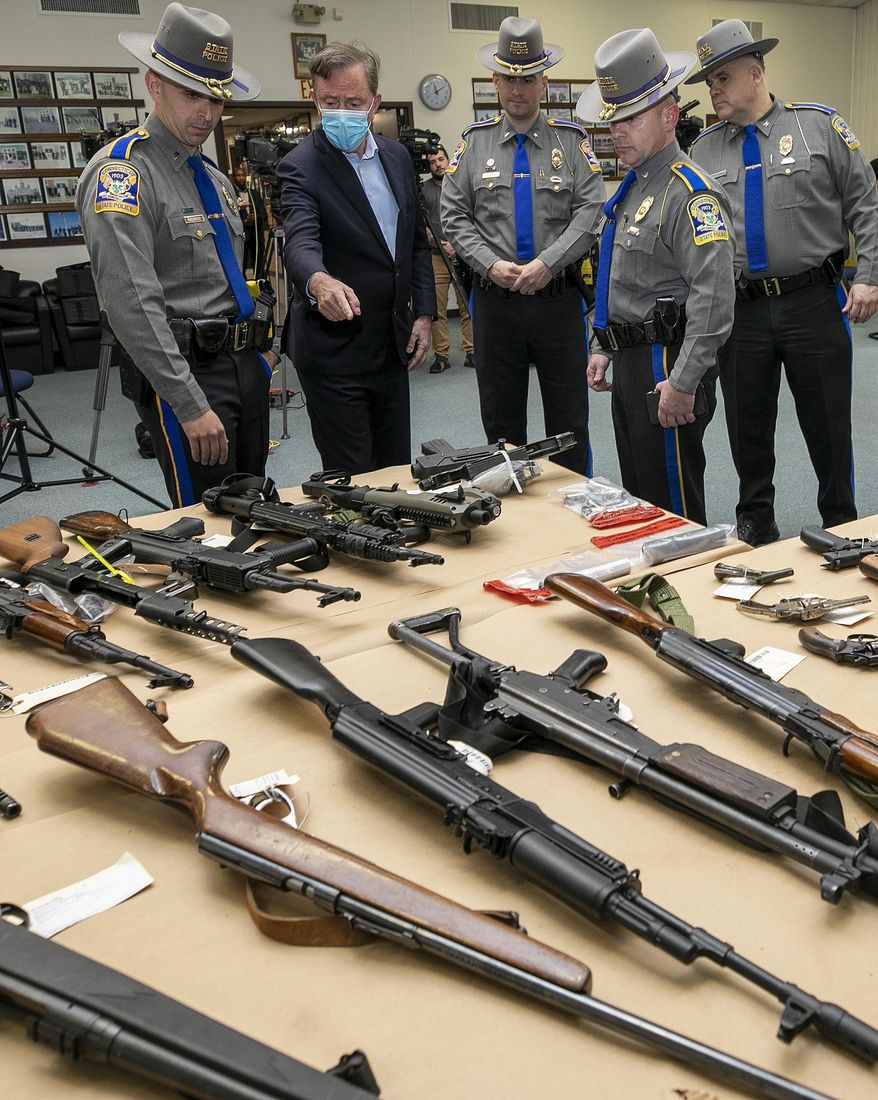 Gov. Ned Lamont and state troopers view dozens of assault weapons, rifles and handguns displayed on a table prior to a press conference at the Connecticut Forensic Science Laboratory in Meriden, Conn. (Dave Zajac/Record-Journal via AP, File)