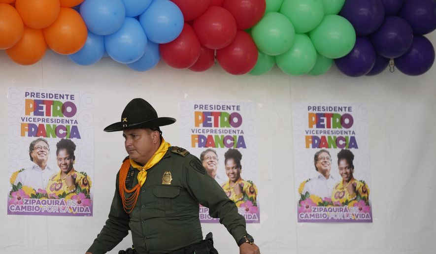 A police officer walks past posters of Historical Pact coalition presidential candidate Gustavo Petro and his running mate Francia Marquez during a closing campaign rally in Zipaquira, Colombia, Sunday, May 22, 2022. Elections are set for May 29. (AP Photo/Fernando Vergara)