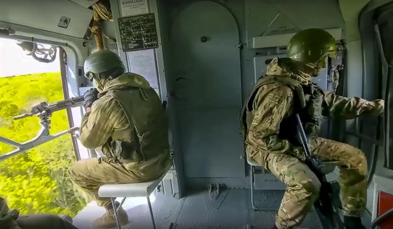 In this handout photo released by the Russian Defense Ministry Press Service released on Saturday, May 28, 2022, Russian soldiers control the situation sitting on a board of a Mi-8 helicopter of the Russian air force during a mission at an undisclosed location in Ukraine. (Russian Defense Ministry Press Service via AP)