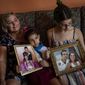 Danmara Triana, left, with her daughters Alice, center, and Claudia, show photos of them with their brother and father who moved to the United States in 2015, at their home in Cienfuegos, Cuba, Thursday, May 19, 2022. Separated families see hope in the measures announced by the U.S. administration of President Joe Biden, but the long wait of years and a web of political interests also makes them skeptical. (AP Photo/Ramon Espinosa)