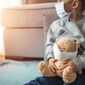 Child and his teddy bear both in protective medical masks sit on windowsill, looking out a window.  Photo credit: Dragana Gordic via Shutterstock