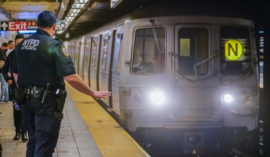 As a subway train enters the Canal St. Q and N station, a NYPD transit officer from the anti terrorism unit gestures to the driver, Tuesday, May 24, 2022, in New York. In the aftermath of a mass shooting on the subway, New York Mayor Eric Adams has floated a high-tech idea of deploying scanners that can spot someone carrying a gun into the transit system before they have a chance to use it. (AP Photo/Mary Altaffer, File)