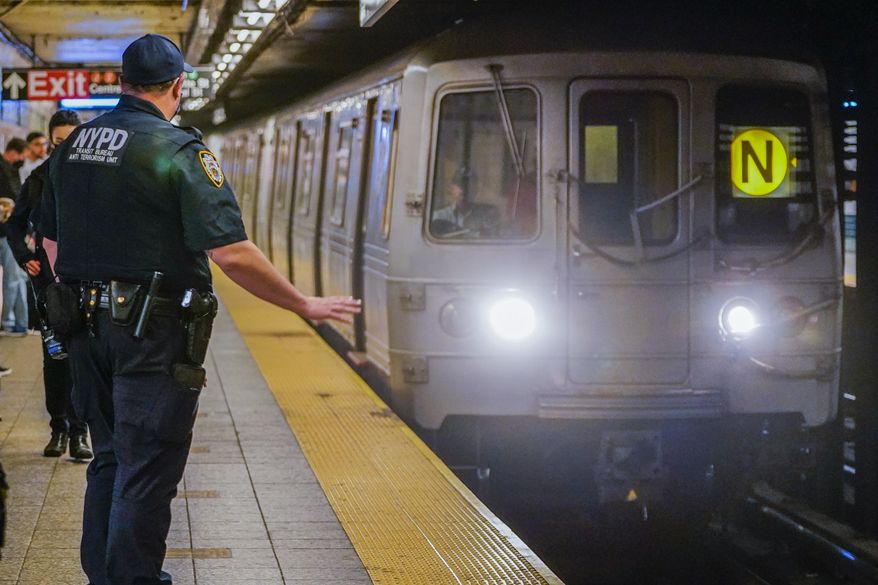 As a subway train enters the Canal St. Q and N station, a NYPD transit officer from the anti terrorism unit gestures to the driver, Tuesday, May 24, 2022, in New York. In the aftermath of a mass shooting on the subway, New York Mayor Eric Adams has floated a high-tech idea of deploying scanners that can spot someone carrying a gun into the transit system before they have a chance to use it. (AP Photo/Mary Altaffer, File)