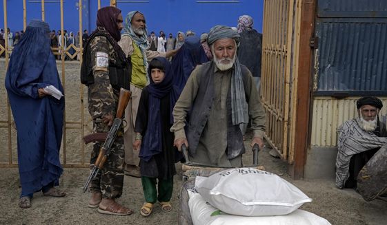 A Taliban fighter stands guard as people receive food rations distributed by a South Koren humanitarian aid group, in Kabul, Afghanistan, Tuesday, May 10, 2022. Afghanistan is expected 1.1 million children under the age of 5 will face malnutrition in the country by the end of this year, as hospitals wards are packed with sick children for sever hunger and malnutrition. (AP Photo/Ebrahim Noroozi)