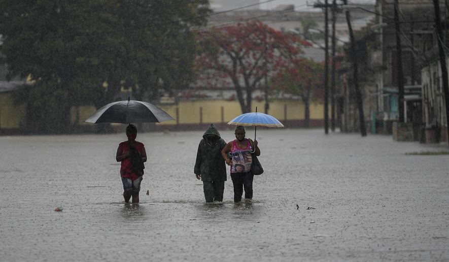 Residents wade through a street flooded by heavy rains, in Havana, Cuba, Friday, June 3, 2022. Heavy rains have drenched Cuba with almost non-stop rain for the last 24 hours as tropical storm watches were posted Thursday for Florida, Cuba and the Bahamas as the system that battered Mexico moves to the east. (AP Photo/Ramon Espinosa)