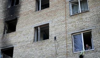 A woman looks outside her window at a building destroyed by attacks in Gorenka, on the outskirts of Kyiv,  Ukraine, Wednesday, June 8, 2022. (AP Photo/Natacha Pisarenko)
