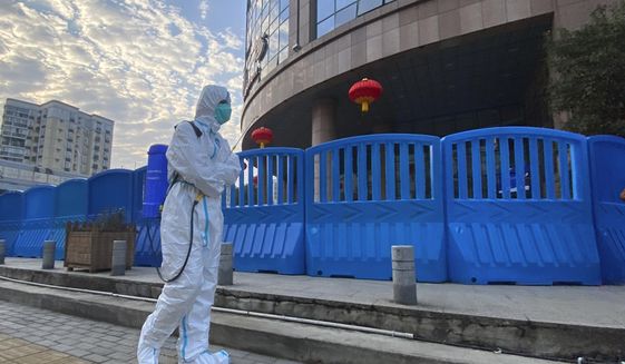 FILE - A worker in protectively overalls and carrying disinfecting equipment walks outside the Wuhan Central Hospital, China on  Feb. 6, 2021. Experts drafted by the World Health Organization to help investigate the origins of the coronavirus pandemic say further research is needed to determine how COVID-19 first began. They say they need a more detailed analysis of the possibility it was a laboratory accident. (AP Photo/Ng Han Guan, File)