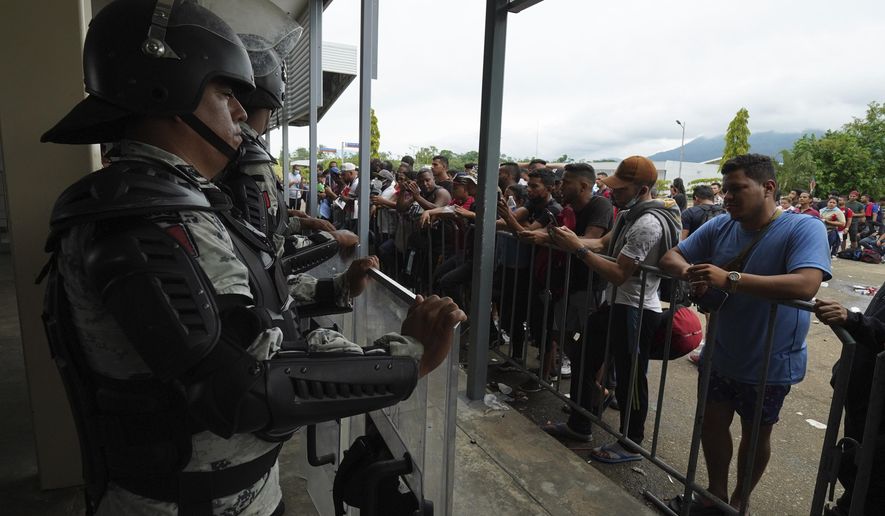 Migrants gather outside the Border Transit Comprehensive Care Center, guarded by security forces, to ask for legal documents that allow them to travel through Mexico, on the outskirts of Huixtla, Chiapas state, Mexico, Friday, June 10, 2022. The group left Tapachula this Monday, tired of waiting to normalize their status in a region with little work, with the ultimate goal of reaching the US. (AP Photo/Marco Ugarte)