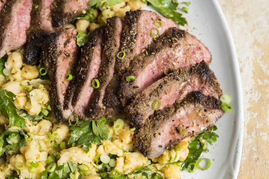 This image released by Milk Street shows a recipe for Spice-Crusted Steak with a side of partially mashed chickpeas. (Milk Street via AP)