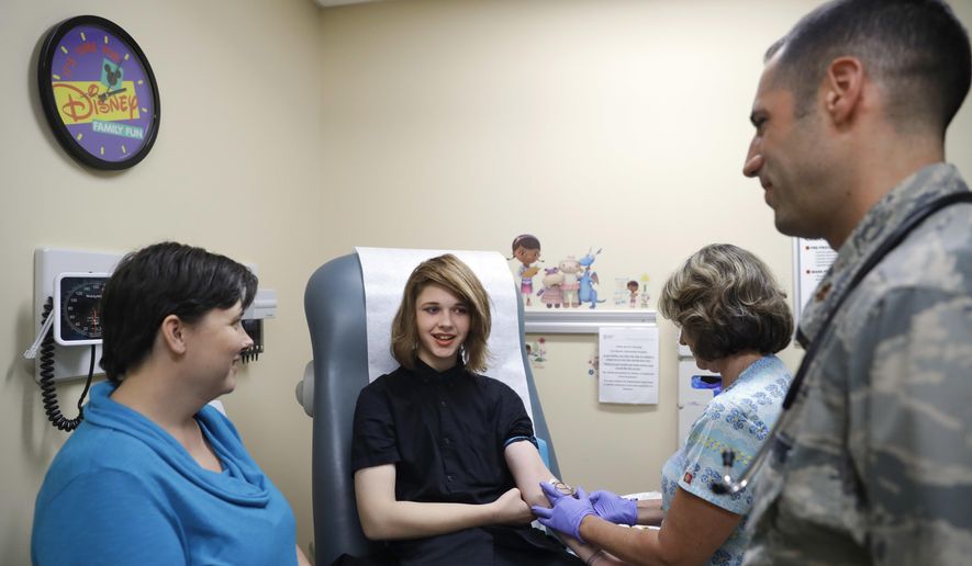 Dr. David Klein, right, an Air Force Major and chief of adolescent medicine at Fort Belvoir Community Hospital, listens as Amanda Brewer, left, speaks with her daughter, Jenn Brewer, 13, as the teenager has blood drawn during a monthly appointment for monitoring her treatment at the hospital in Fort Belvoir, Va., on Sept. 7, 2016. Brewer is transitioning from male to female. (AP Photo/Jacquelyn Martin, File)