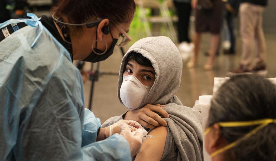 In this May 24, 2021, photo, a student looks back at his mother as he is vaccinated at a school-based COVID-19 vaccination clinic for students 12 and older in San Pedro, Calif. (AP Photo/Damian Dovarganes) **FILE**