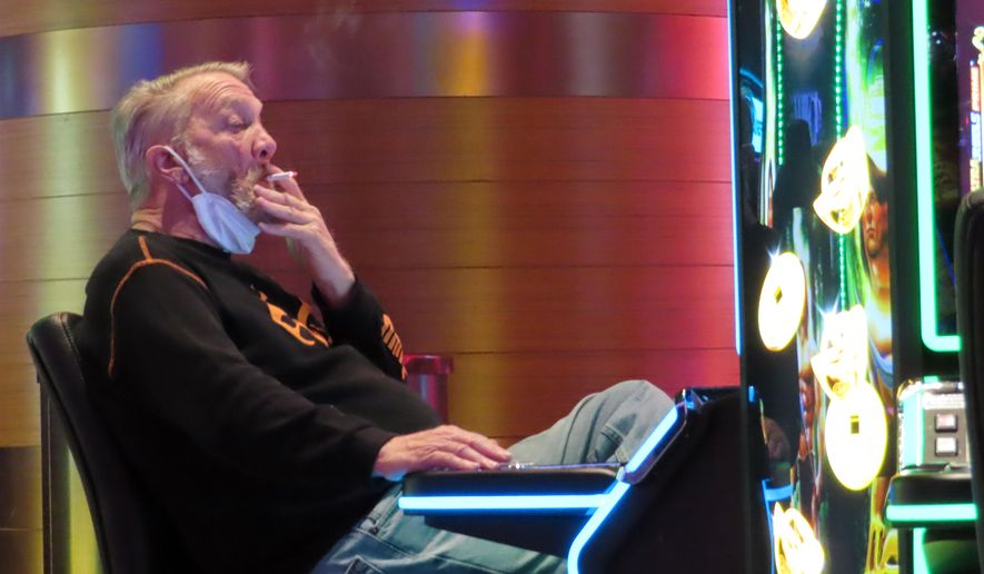 A man smokes while playing a slot machine at the Ocean Casino Resort in Atlantic City, N.J., on Feb. 10, 2022. A report issued Friday, June 17, 2022, by a Las Vegas gambling research company suggested that ending smoking in casinos will not result in significant financial harm to the businesses. (AP Photo/Wayne Parry, File)