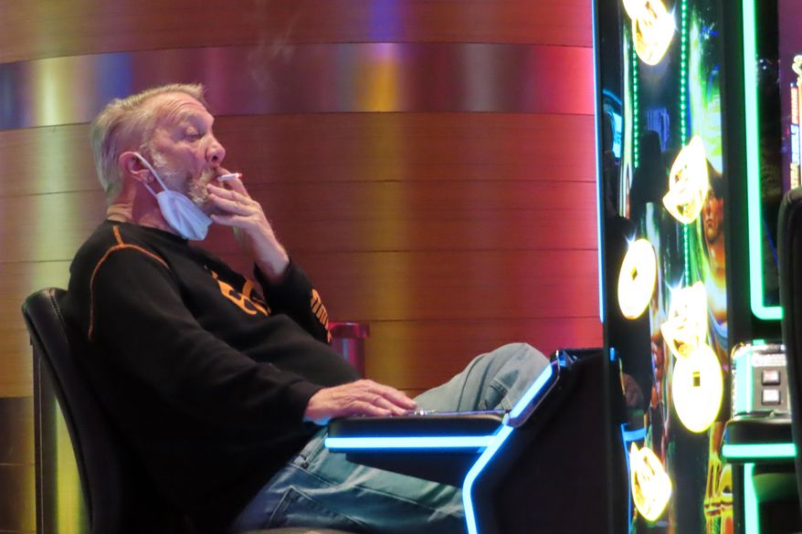 A man smokes while playing a slot machine at the Ocean Casino Resort in Atlantic City, N.J., on Feb. 10, 2022. A report issued Friday, June 17, 2022, by a Las Vegas gambling research company suggested that ending smoking in casinos will not result in significant financial harm to the businesses. (AP Photo/Wayne Parry, File)